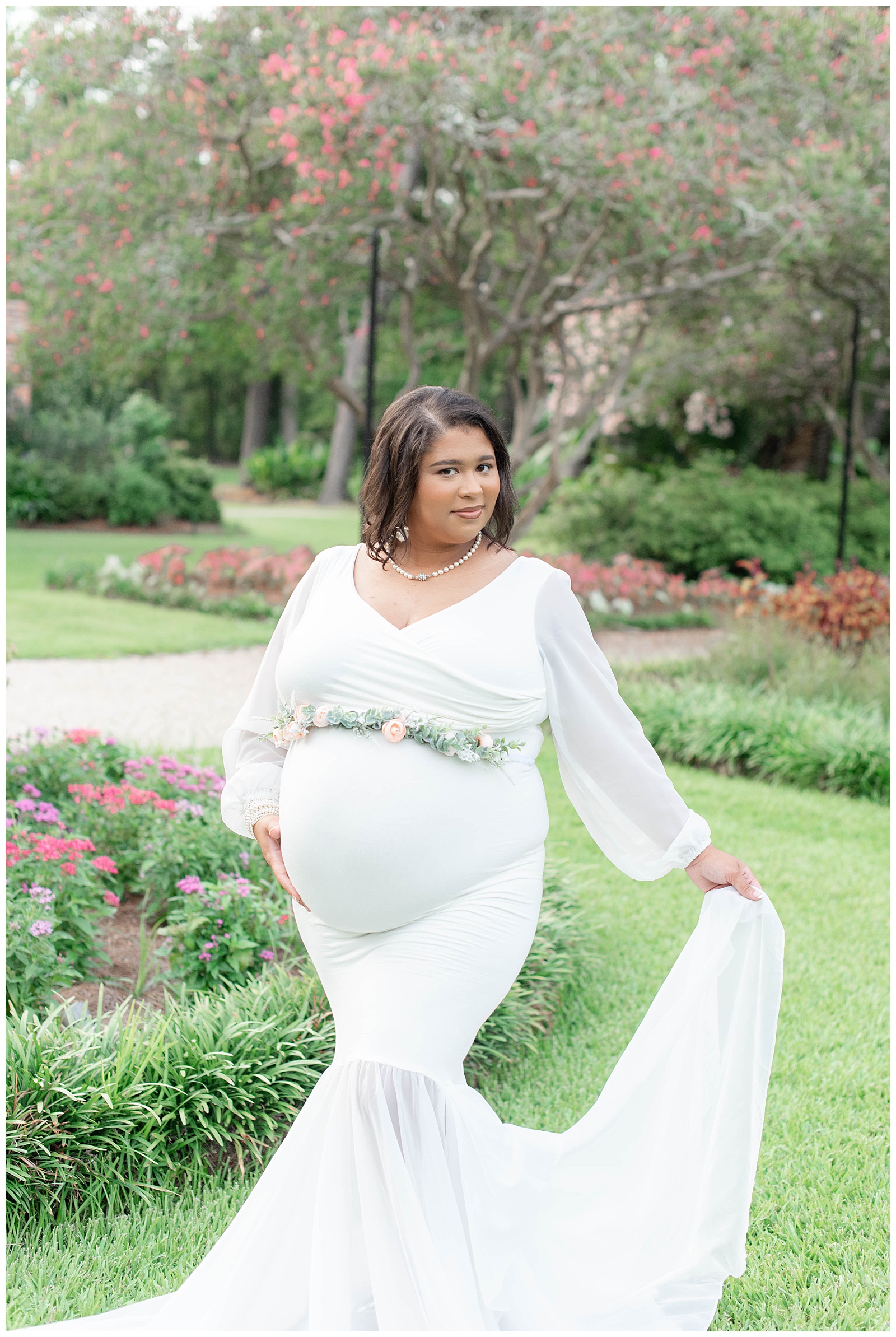 mom holds white dress and belly in the rose garden at Burden Center