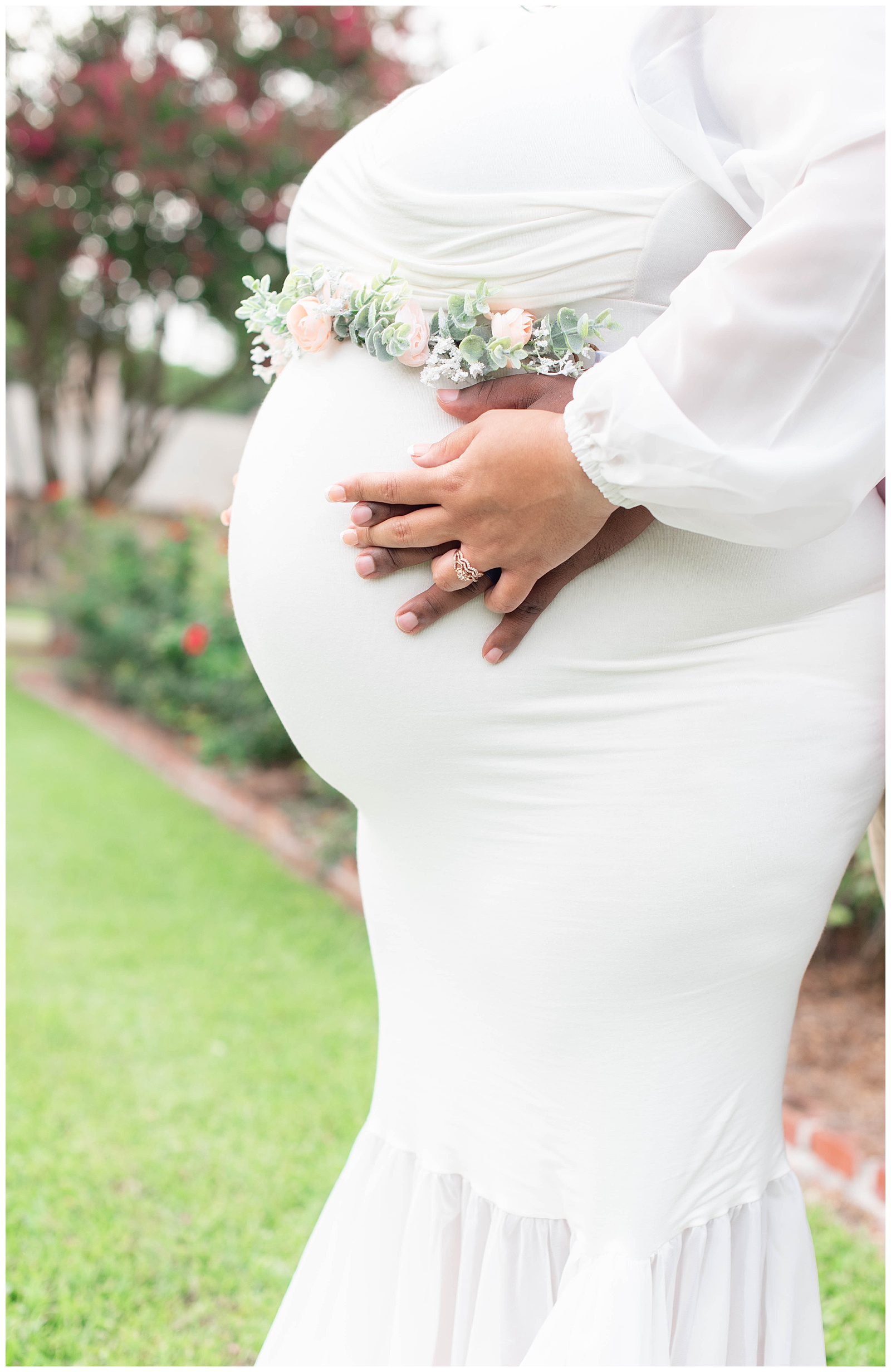 husband and wife holds hands and show off baby bump in the rose garden at Burden Center