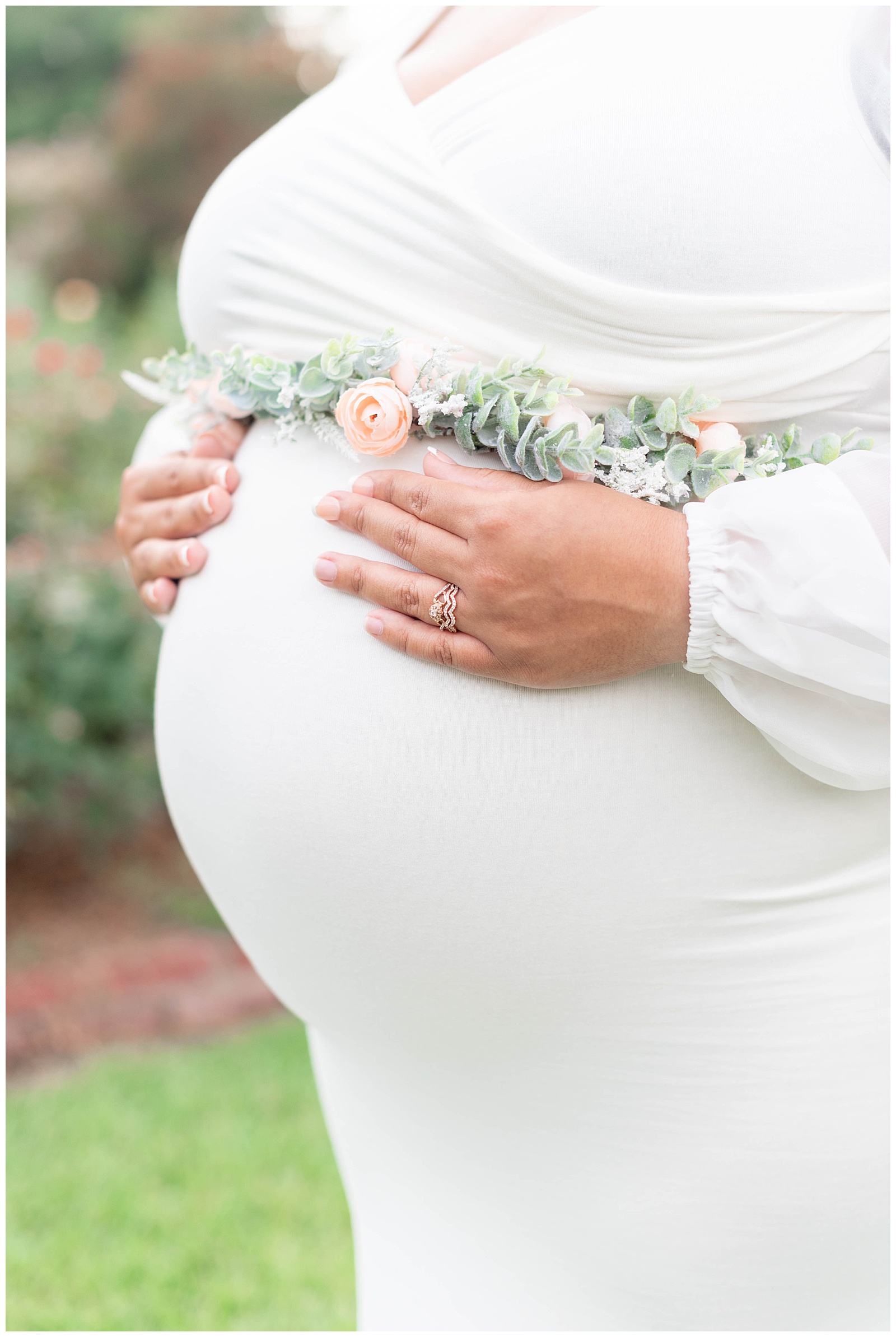 moms hand on her baby bump in the rose garden at Burden Center