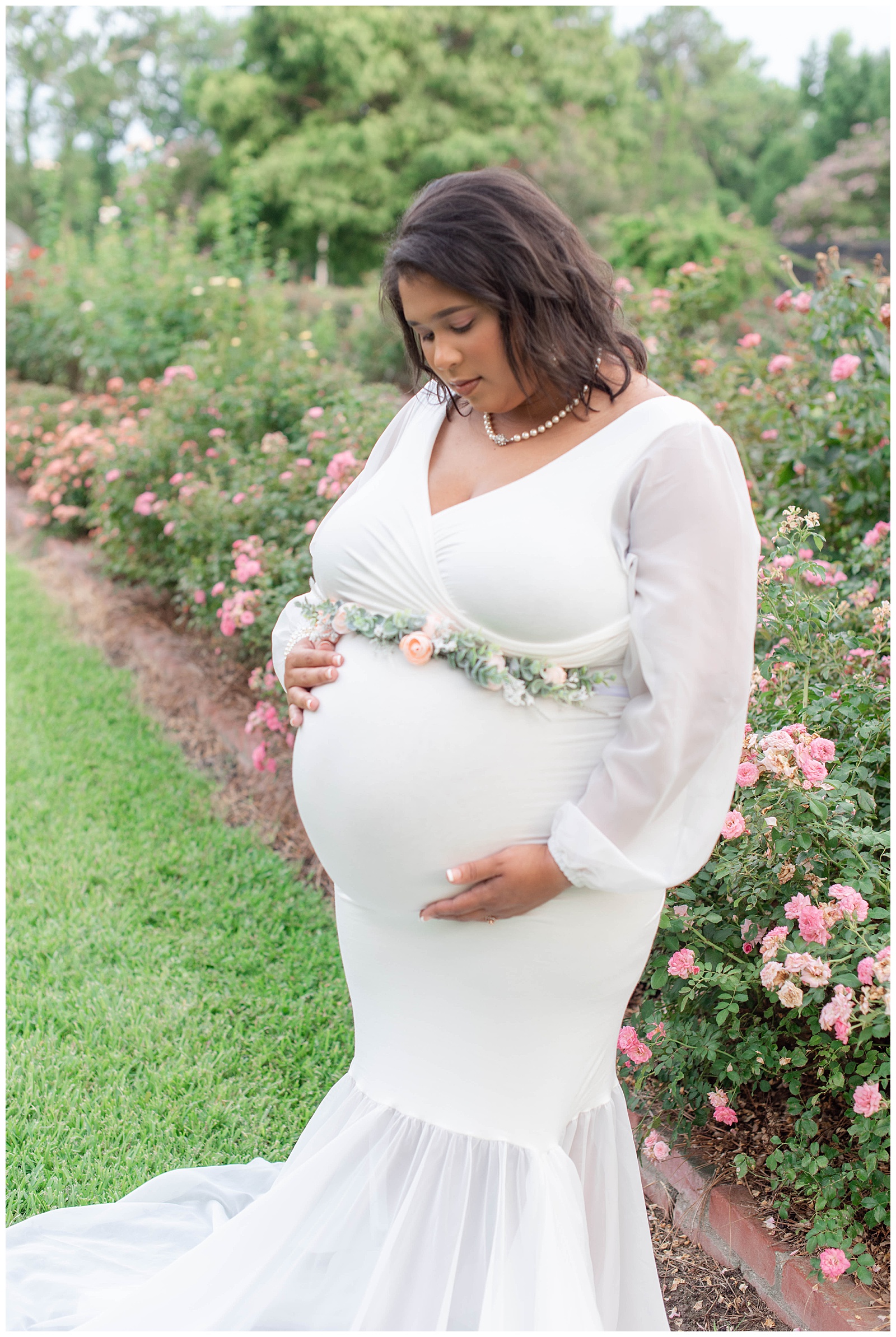 mom glances at belly in rose garden at Burden Center