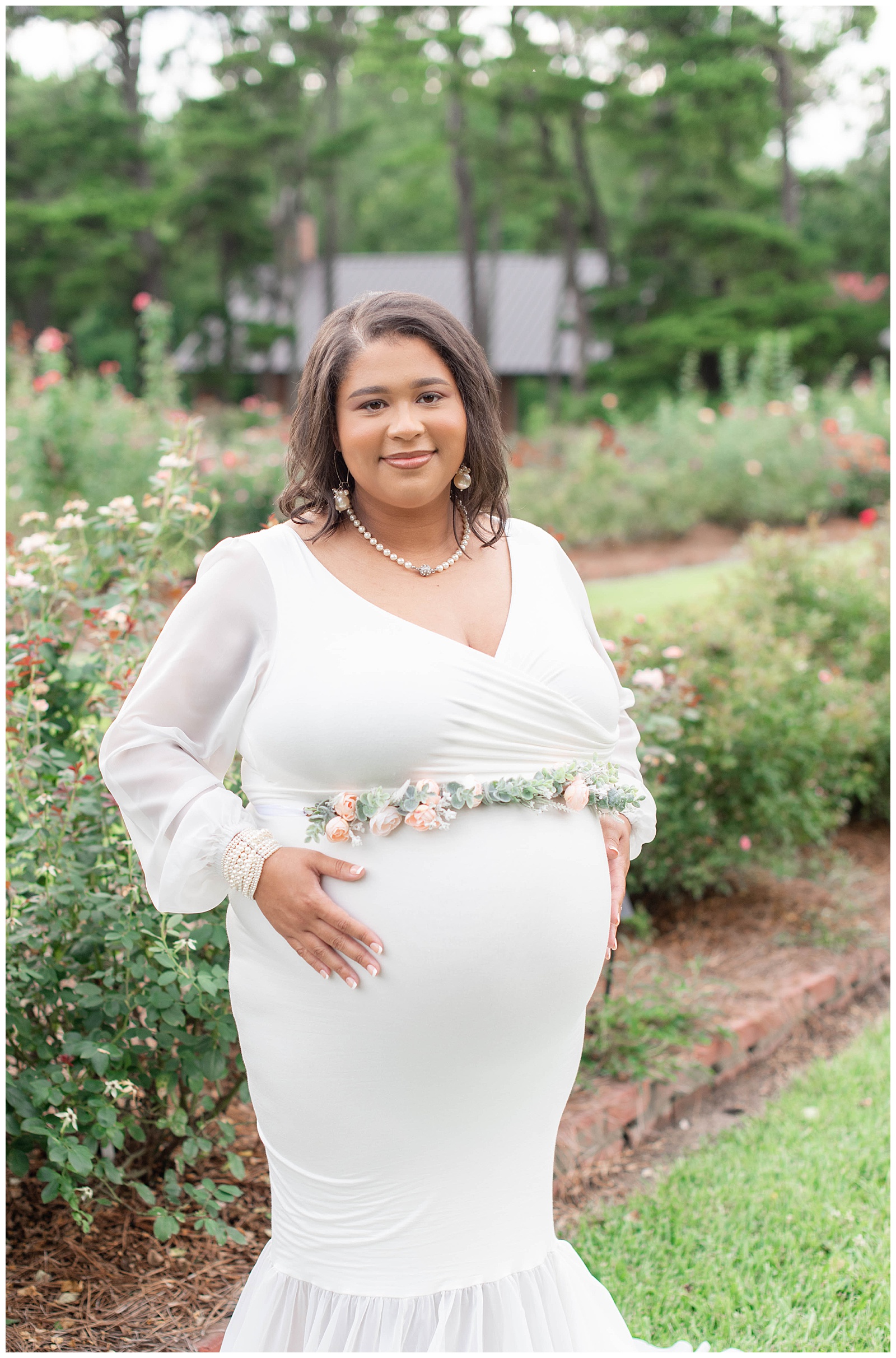 mom to be smiles gives a subtle smile in rose garden at Burden Center