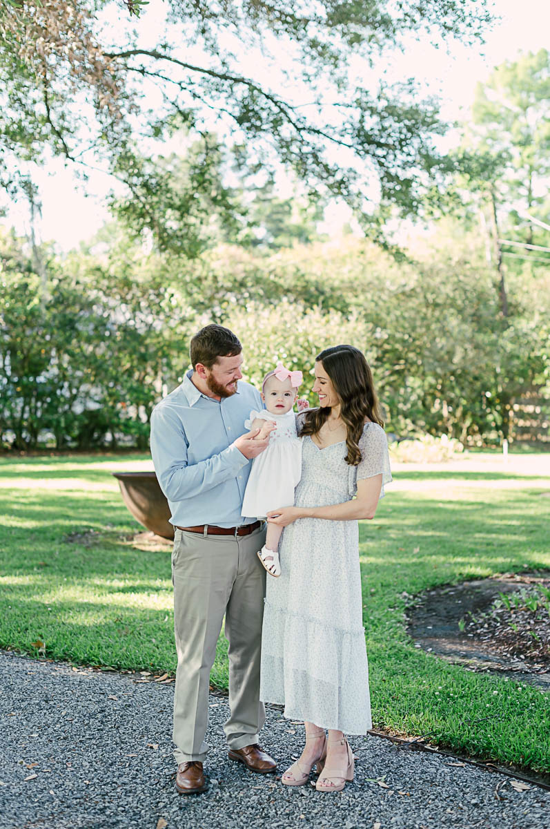 mom and dad hold one year old on hip during outdoor first birhtday session with Amanda Higgins